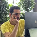 Mahdi in a yellow polo and clear glasses, chin on his hand, looking at a laptop.